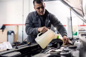 auto-mechanic-is-pouring-oil-into-car-engine-hood-while-standing-garage