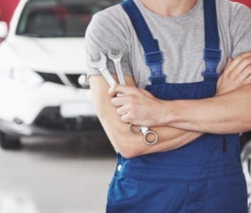 Fleet service technician holding wrenches in front of a vehicle.