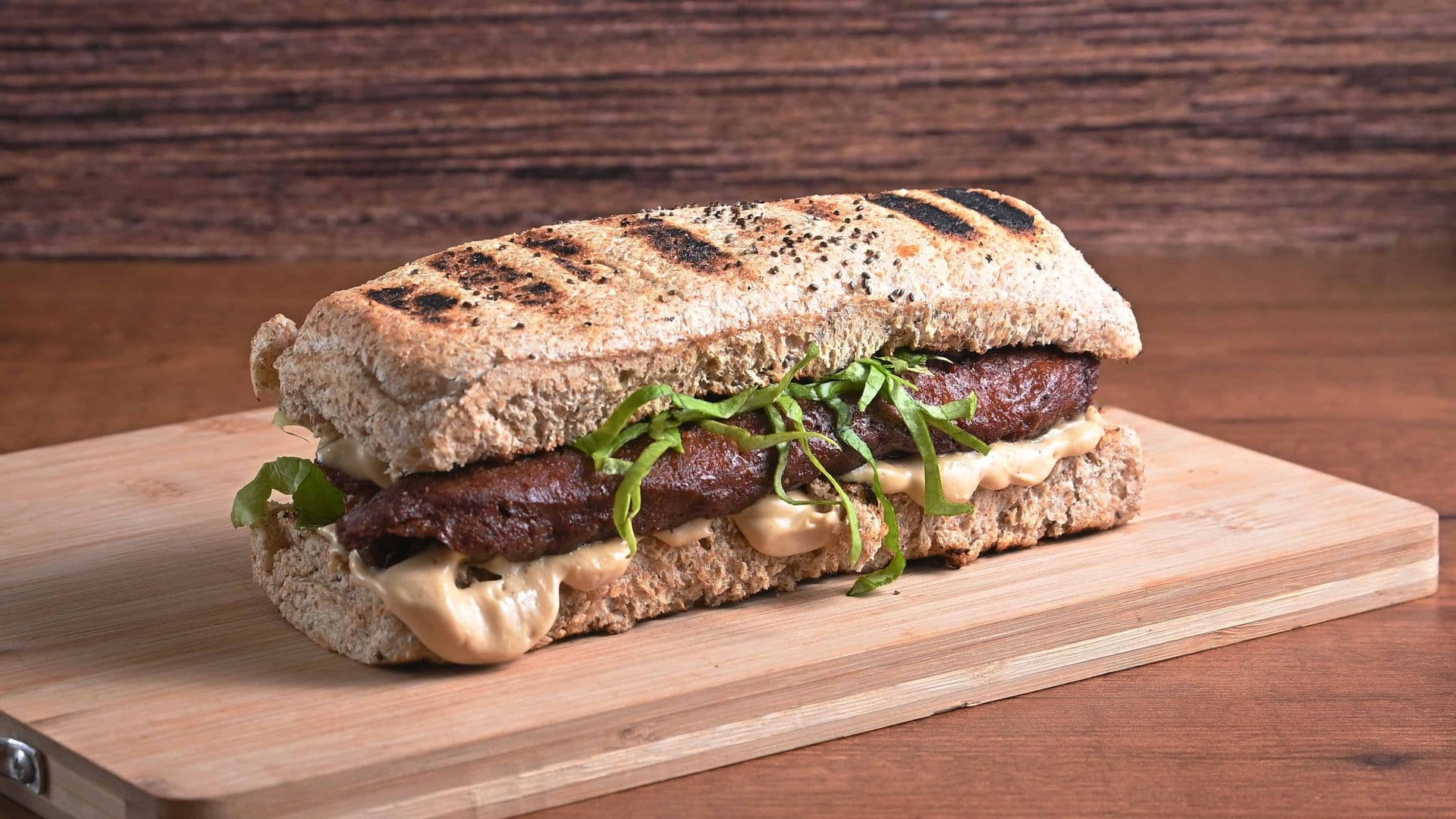 Ukusan hot dog sa mesom, sirom i salatom na drvenoj dasci.