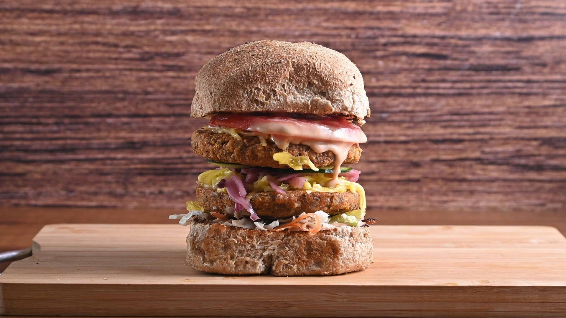Ukusan Šefov burger sa slojevima mesa, povrća i sosa na drvenoj podlozi.