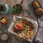 Falafel burger sa svežim povrćem i pomfritom na drvenom stolu.