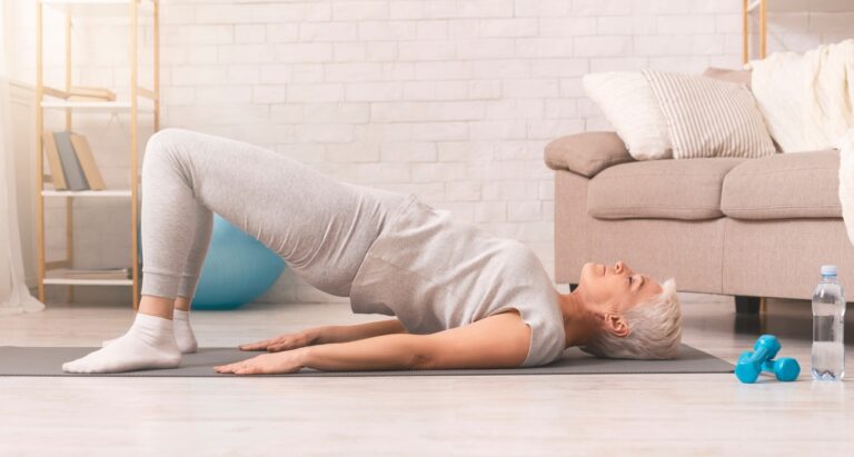 Elderly woman performing gentle glute bridge exercise on yoga mat for nerve pain relief, promoting neuropathy management and overall health.