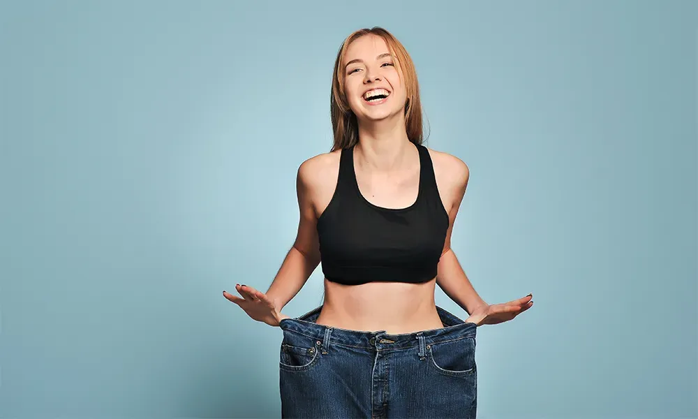 Happy woman showing off loose jeans after weight loss, representing successful medical weight management with Tirzepatide in Mexico.