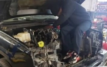 Automotive mechanic working on car engine at Rob & Son Garage, specializing in engine repairs and ve.
