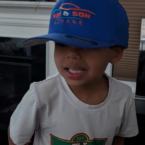 Young boy wearing a blue Rob & Son Garage cap and white T-shirt.
