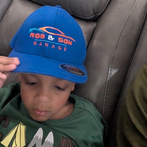 Child wearing Rob & Son Garage branded cap sitting on a couch.
