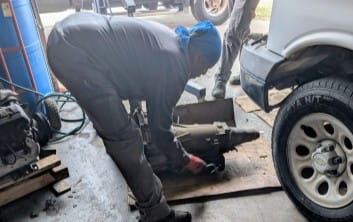 Garage repair technician working on a vehicle under the car.