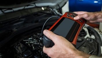 Technician using diagnostic scanner on car engine for auto repair and maintenance.