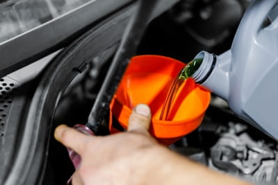 Mechanic pouring engine oil into a car engine during oil change service.