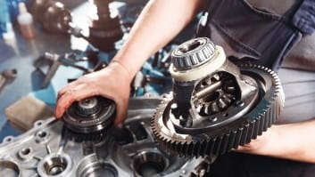 Close-up of a mechanic's hands working on car transmission gears and components.