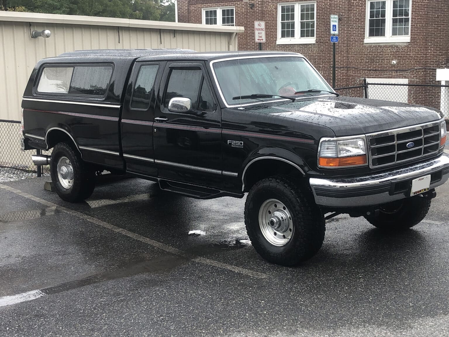 Ford F-150 pickup truck with camper shell, parked in front of auto repair shop.