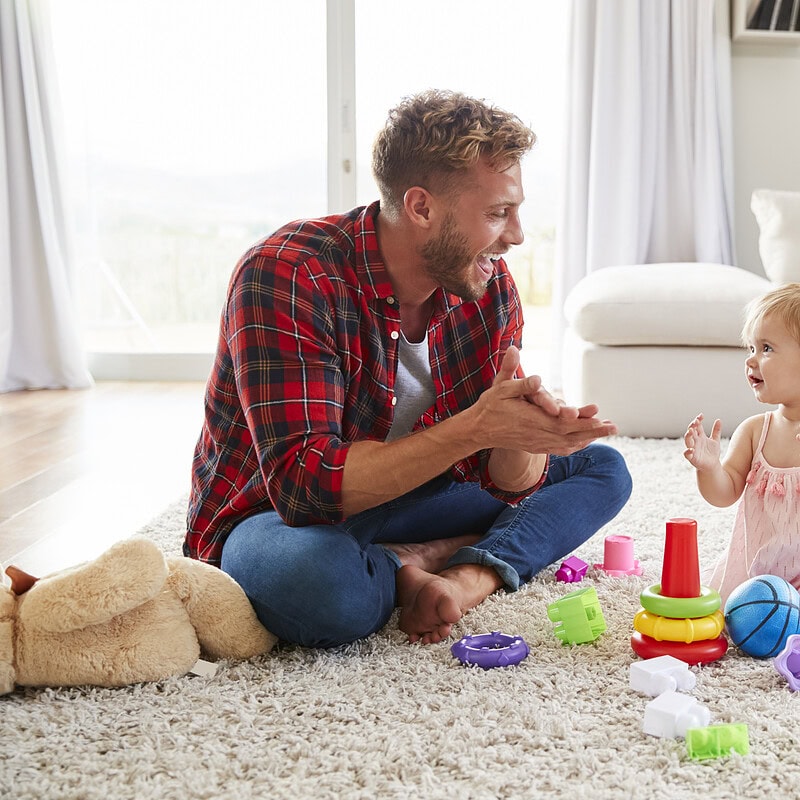 An image that shows Young Father And Toddler Daughter Clapping In Sitting Room