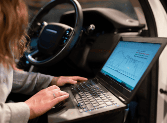Auto repair technician analyzing vehicle diagnostics on a laptop inside a car.
