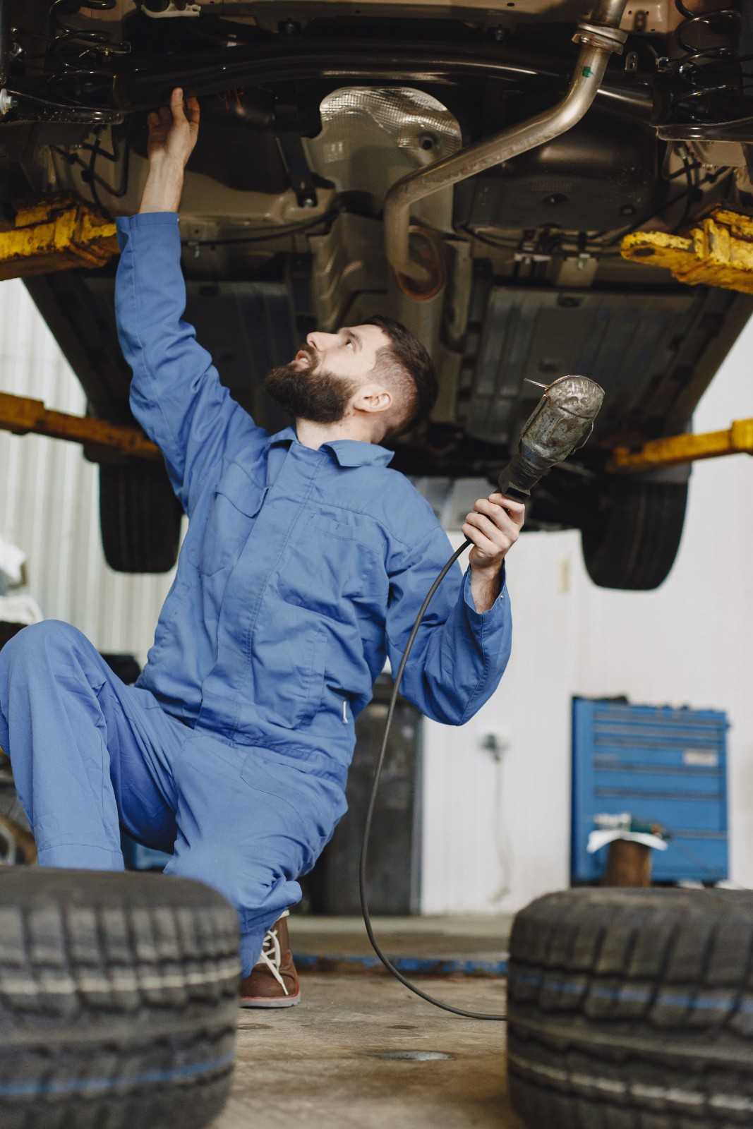 Auto repair technician inspecting under vehicle with tools in garage.
