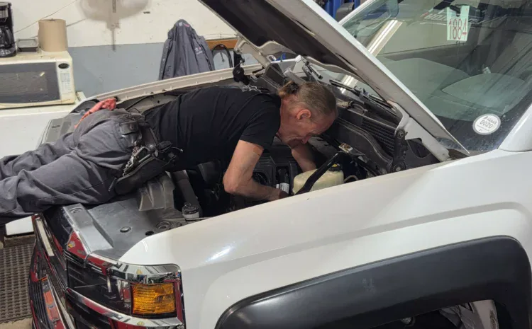 Technician inspecting engine bay of a white vehicle at Sanfelippo Auto Repair.