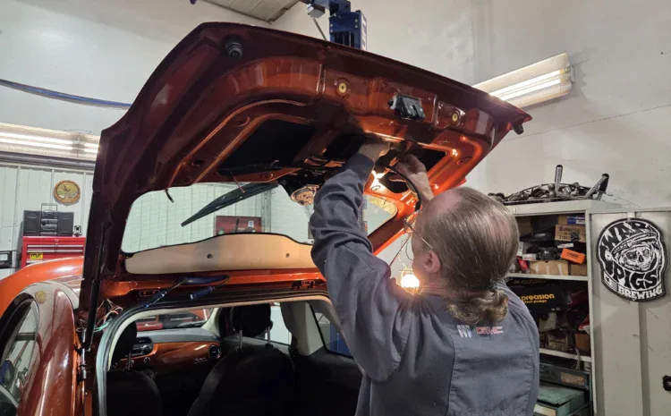 Technician inspecting a car hood at Sanfelippo Auto Repair shop in a garage.