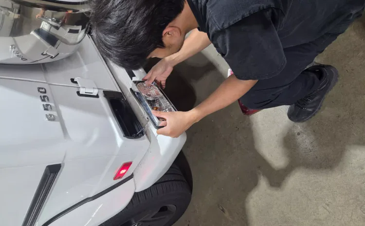Mechanic inspecting a white SUV's front area during repair.