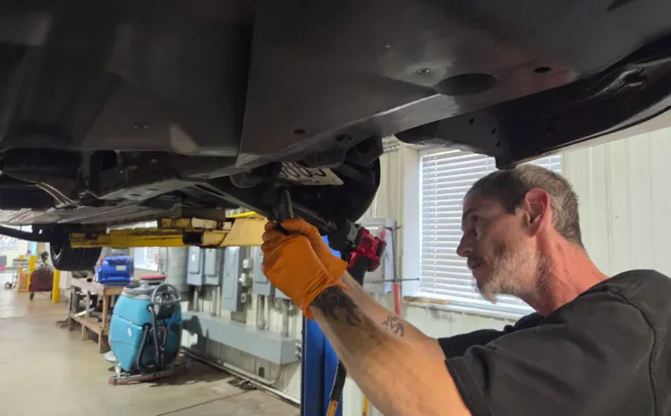 Auto repair technician inspecting vehicle underside in shop bay.