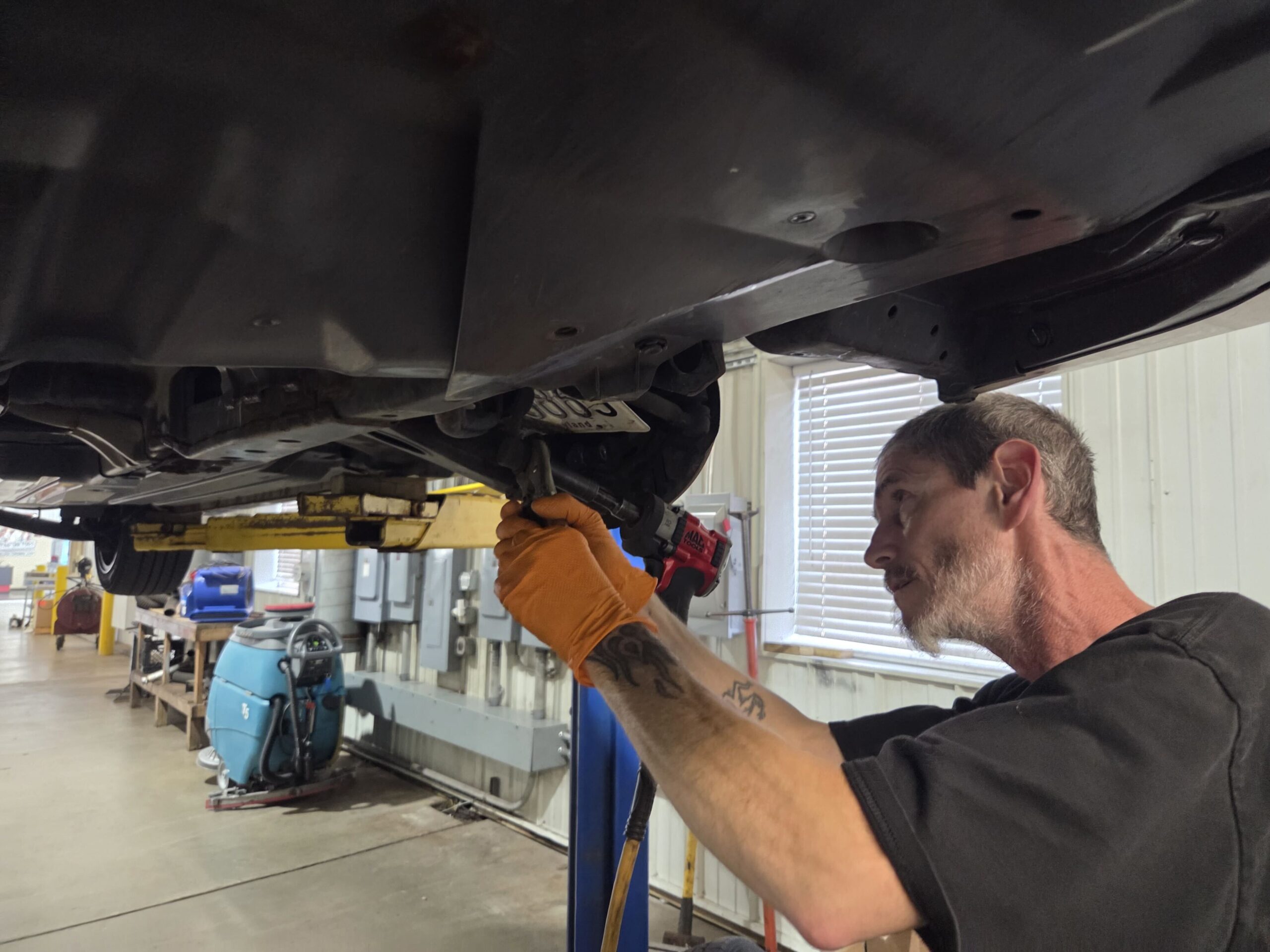 Auto mechanic inspecting under vehicle for alignment and tire issues.