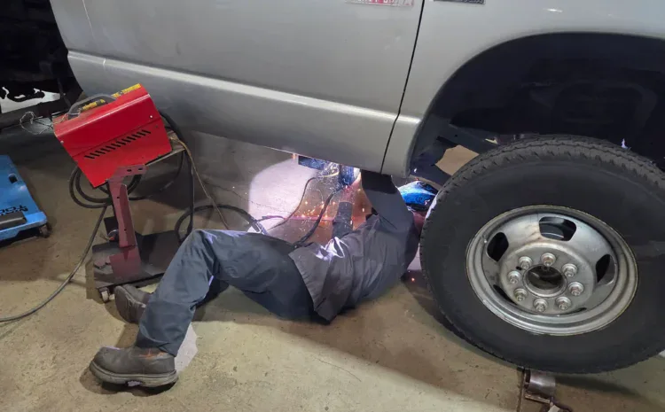 Auto repair technician working under a lifted truck at a shop.