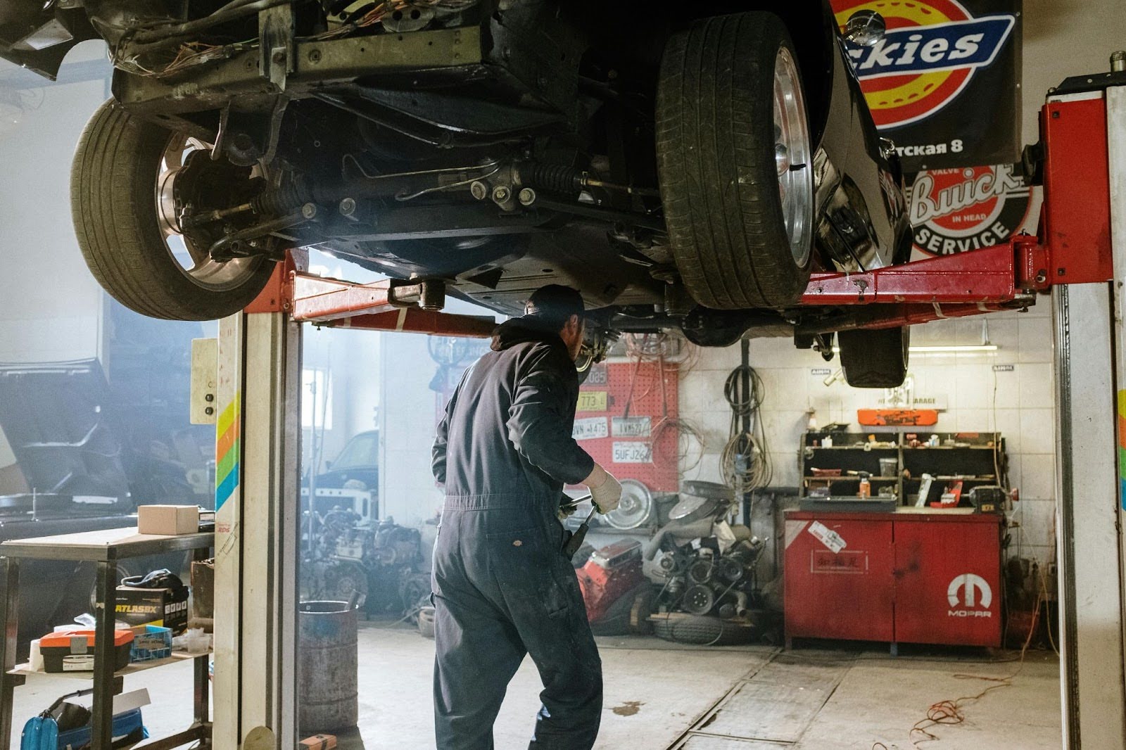 Car repair technician inspecting vehicle on hydraulic lift.