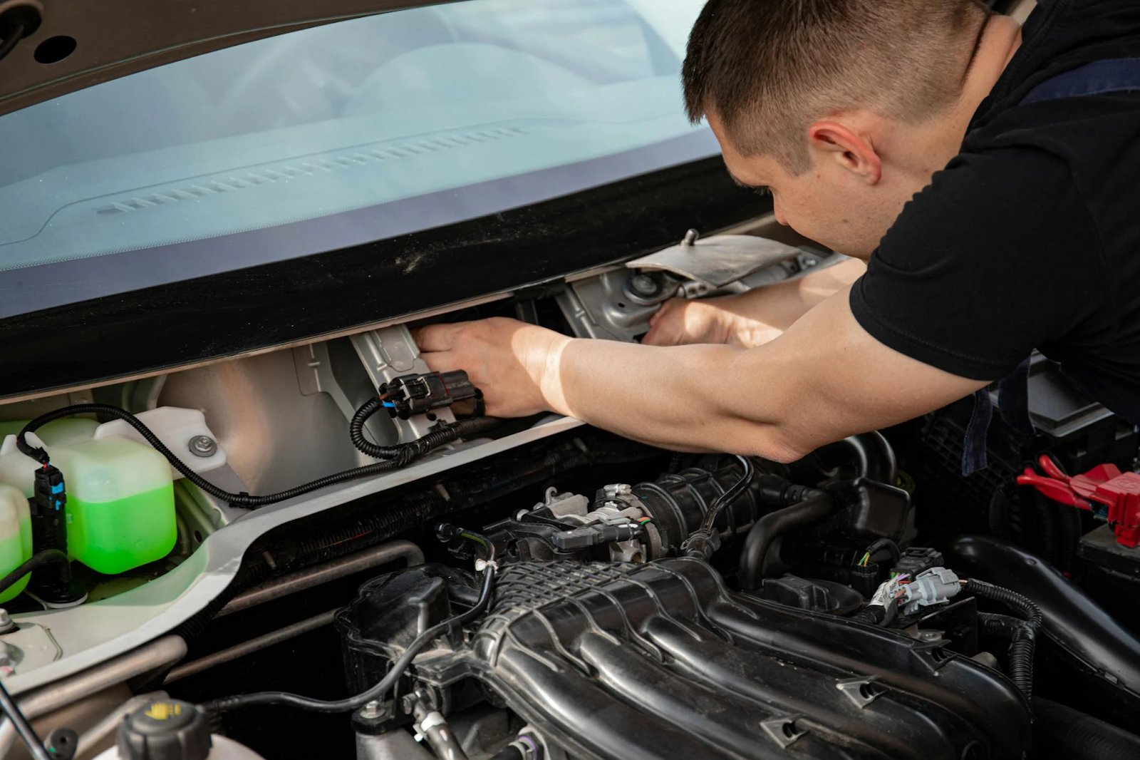 Technician inspecting a car engine for transmission problems under the hood.