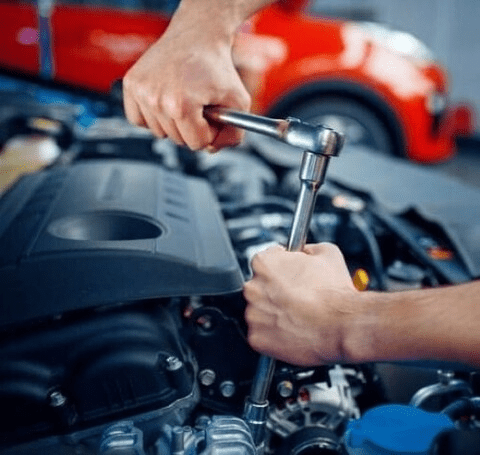Mechanic working on car engine with tools in garage.