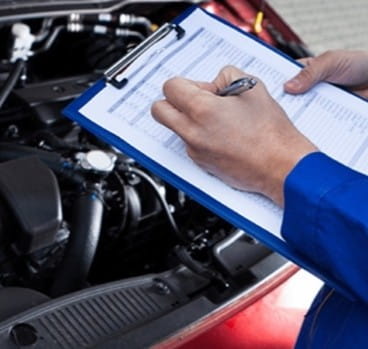 Technician inspecting car engine with clipboard for vehicle maintenance.