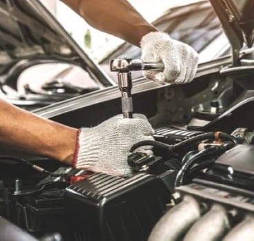 Mechanic repairing car engine with tools at Schimpfs Garage.