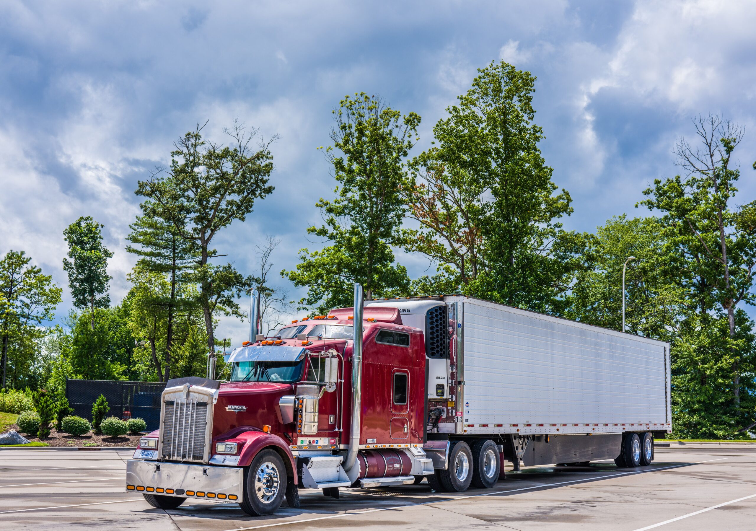 Red semi truck with trailer parked in lot, ready for repair or maintenance.