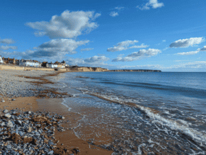 Scenic coastal beach with pebbles, sand, and waves under a blue sky, ideal for seaglass hunting.