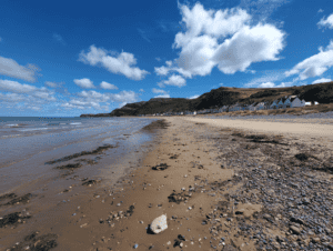 Scenic beach with rocky shoreline and scattered seaglass under a blue sky.