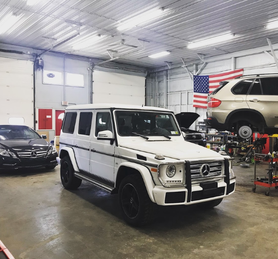 Luxury Mercedes-Benz G-Class SUV inside auto repair shop, with a vehicle lift and American flag in t.