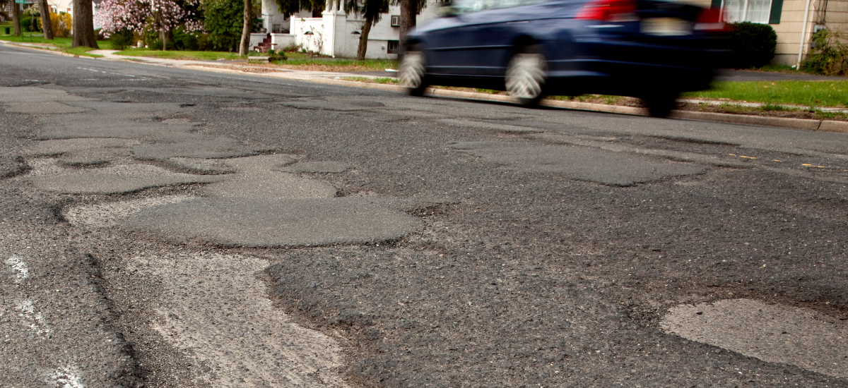 Potholes on a city street highlighting the need for suspension and steering maintenance.