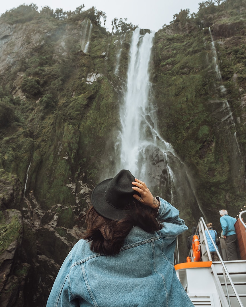A girl standing in front of a waterfall. Milford Sound boat tour. New Zealand South Island