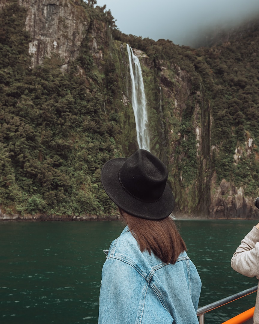 A girl standing in front of a waterfall. Milford Sound boat tour. New Zealand South Island