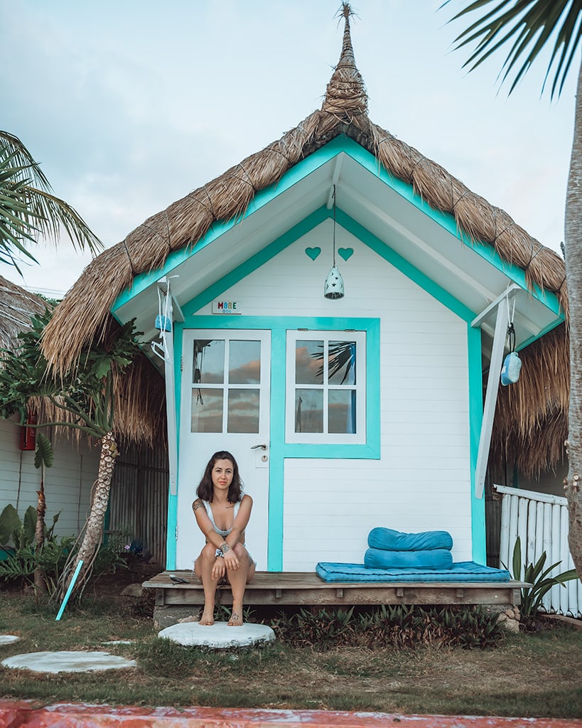 A woman sits outside a charming, small beach hut painted in bright colors with a thatched roof. Le Pirate, Nusa Ceningan.