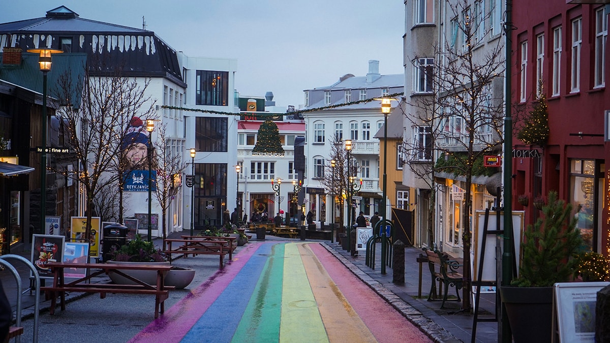 Reykjavik's Rainbow Street with shops either side of the road. There are small golden Christmas lights decorating the shops and a green bell hanging above the street.
