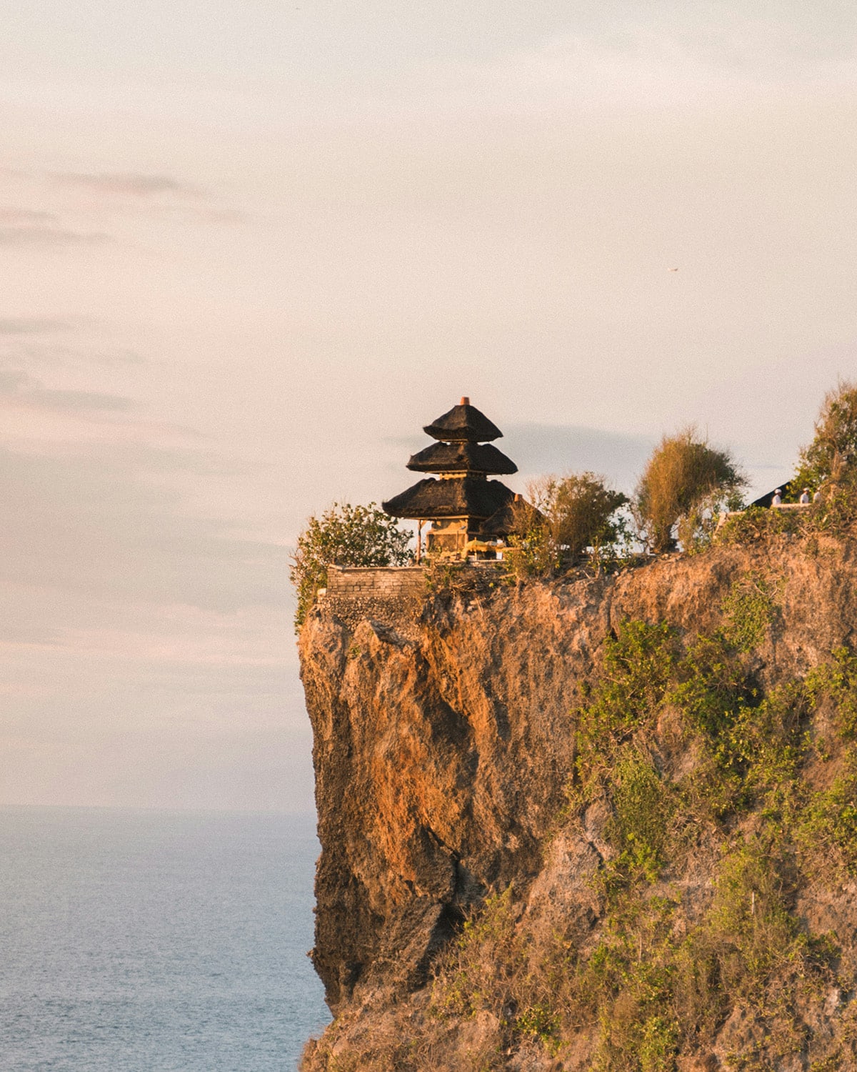 A traditional thatched temple perches precariously on the edge of a high cliff overlooking the ocean. Uluwatu, the first stop on 10 days in Bali itinerary.