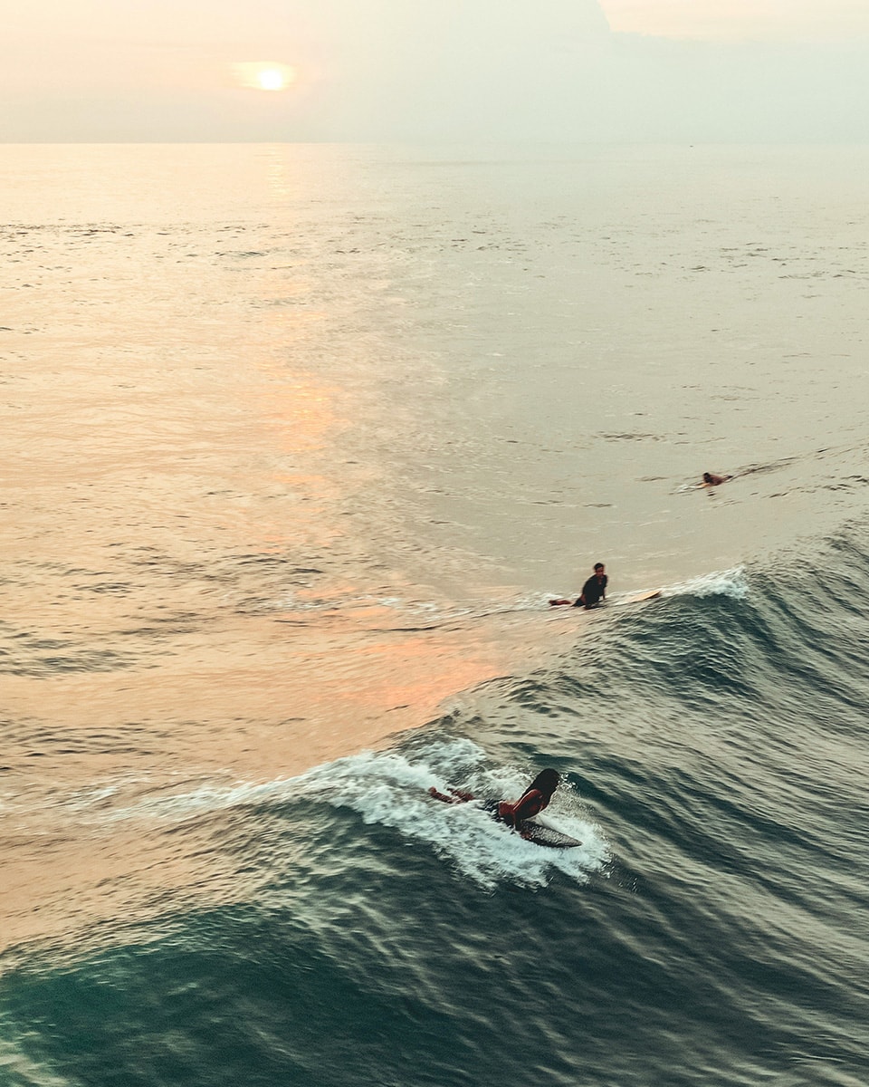 At dusk, a surfer rides a wave with a beautiful sunset illuminating the ocean.