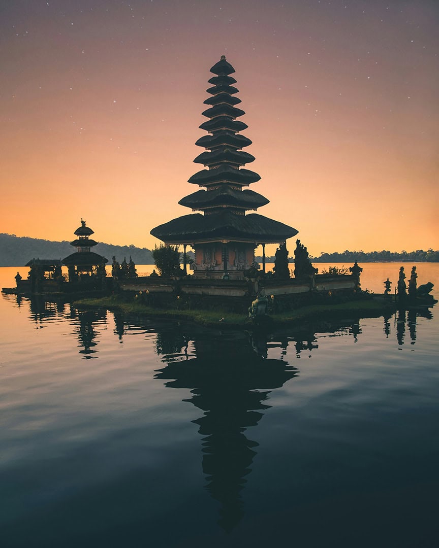 A picturesque temple sits on a lake with a beautiful sunset sky in the background.