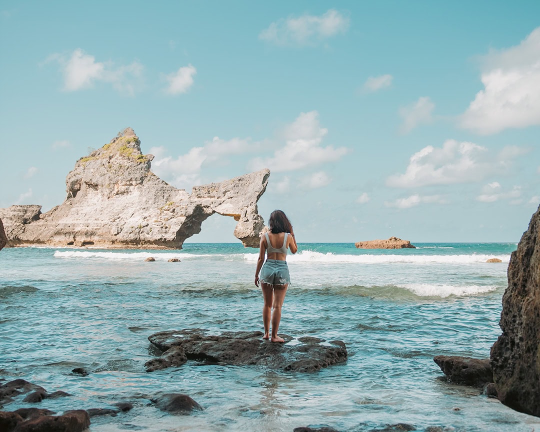A woman standing on rocks at the edge of the water, looking out at the unique rock formations in the sea.
