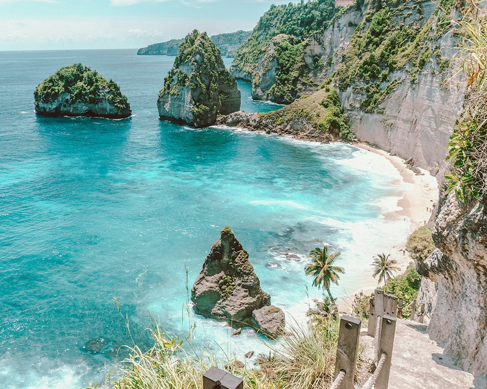 A view of the turquoise waters and rocky outcrops of Diamond Beach in Bali from a staircase descending the cliffs.
