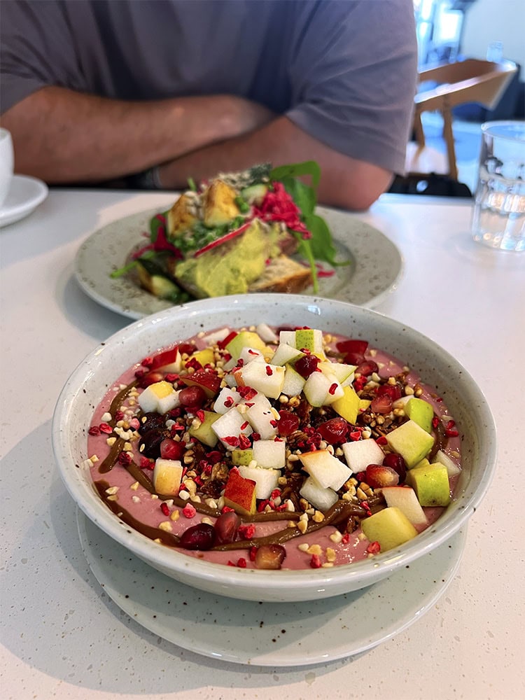 A close-up of a purple smoothie bowl topped with chopped fruits,and nuts with another dish in the background.