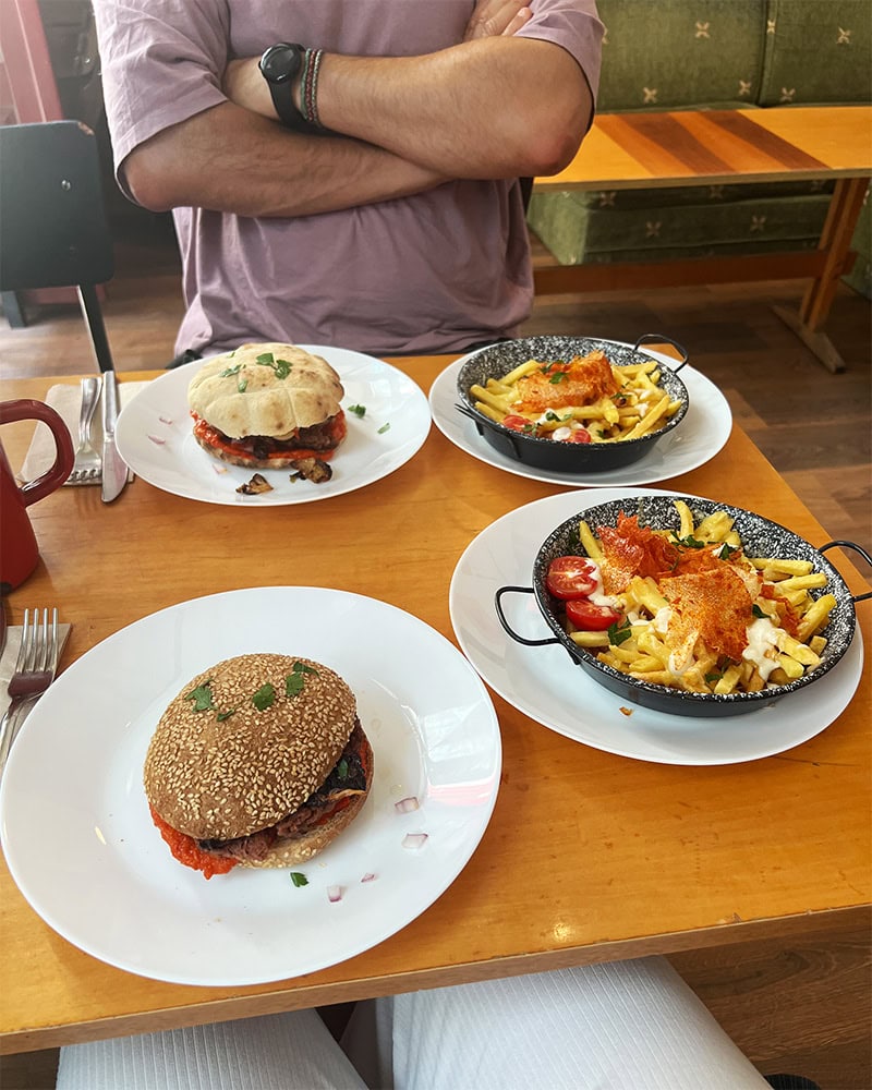 A table set with two burgers and two plates of fries covered in vegan cheese.