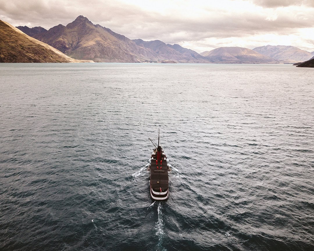 A steamship sailing across a large lake with mountains in the background on a cloudy day.