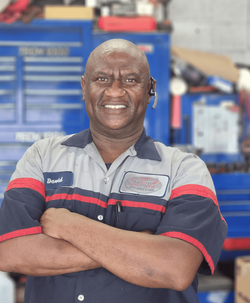 Auto repair technician smiling with arms crossed in workshop.