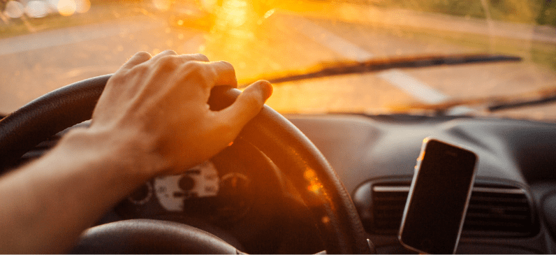 Driver holding steering wheel during sunset, promoting summer vehicle maintenance.