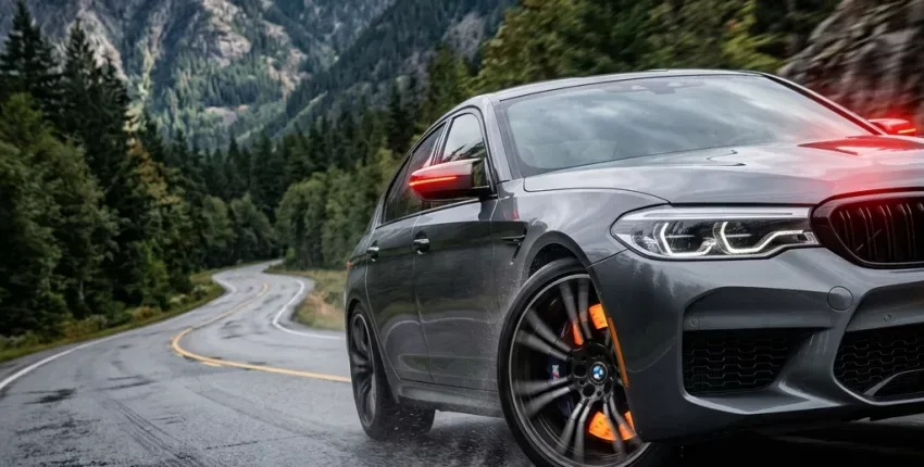 BMW sports car driving on wet mountain road with scenic forest backdrop.