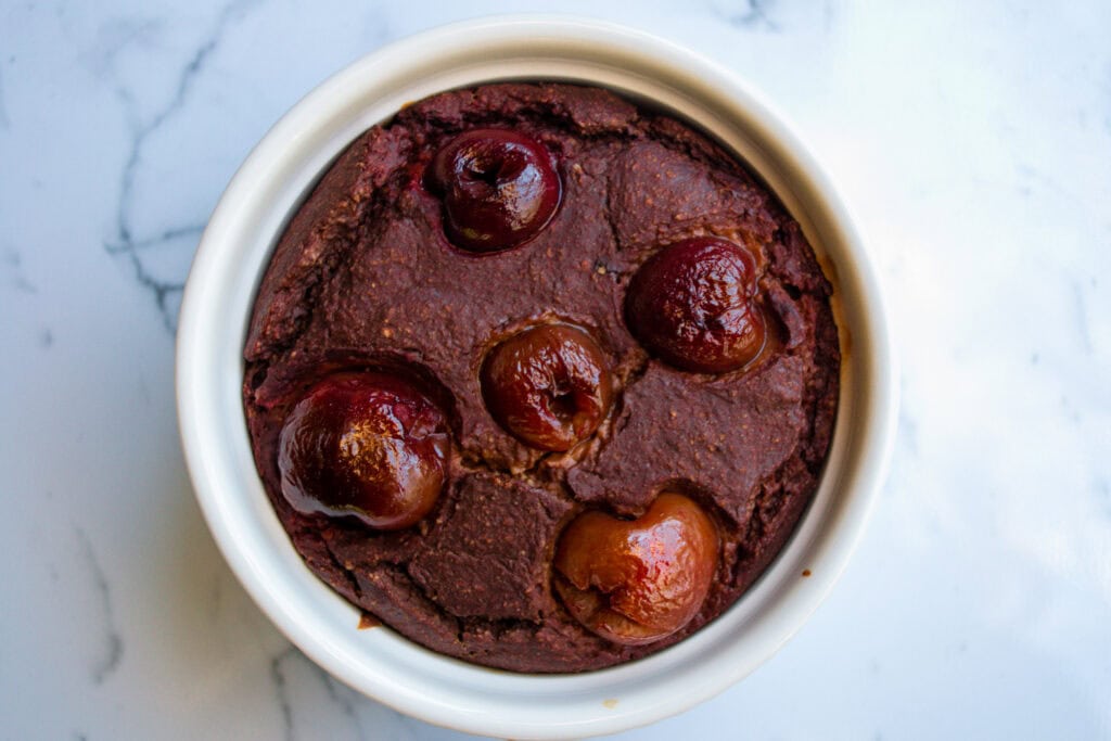 Rich cherry chocolate microwave mug cake in a white ramekin, showcasing a moist, decadent dessert topped with fresh cherries, perfect for quick healthy dessert recipes.